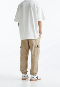 Hvid oversized t-shirt, beige cargo bukser med sidelommer og hvide sneakers med sorte detaljer. Glat tekstur og afslappet pasform.