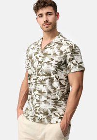 Chemise à manches courtes en tissu léger et texturé, avec un motif abstrait vert et blanc, dotée d'un col en V et d'une fermeture à boutons.