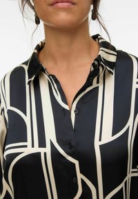 Black and white button-up shirt with geometric patterns, featuring a collar and smooth satin-like texture. Buttons and contrasting designs are visible.