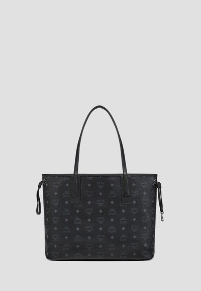 Schwarze Leder-Totetasche mit dunkelgrauem MCM-Logo-Muster, zwei langen Griffen und seitlichen Kordelzugdetails vor einem schlichten grauen Hintergrund.