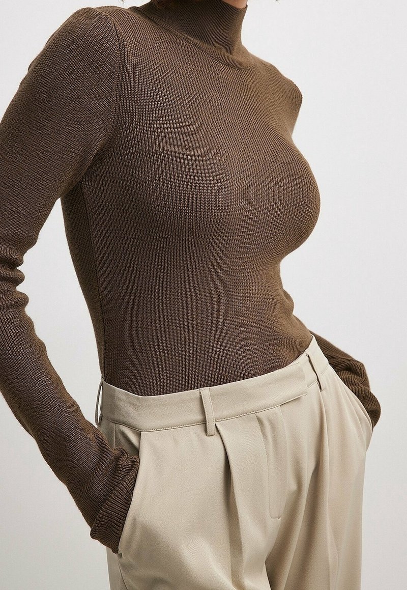 Ruskea ribbineule poolopaita yhdistettynä beigenvärisiin, pliseerattuihin, korkeavyötäröisiin housuihin. Paidassa on pitkät hihat ja vartalonmyötäinen leikkaus.