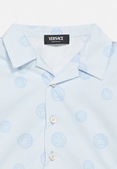 Jasnoniebieska koszula Versace z subtelnym wzorem głowy Meduzy, klasycznym kołnierzykiem, białymi guzikami oraz metką "Made in Italy" wewnątrz kołnierzyka.