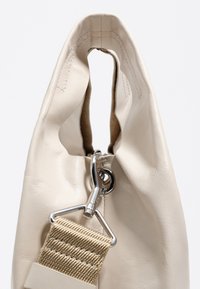 Kremowa torba wykonana z teksturowanego syntetycznego materiału. Posiada duże otwarcie z srebrnym zapięciem oraz beżowy pleciony pasek.
