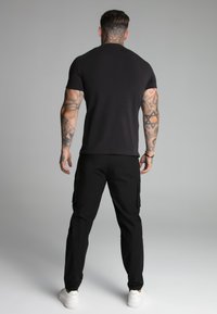 Czarny t-shirt z krótkim rękawem o dopasowanym kroju, w połączeniu z czarnymi spodniami cargo z bocznymi kieszeniami oraz białymi sneakersami.