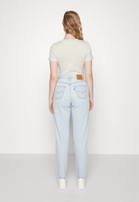 Jeans in denim azzurro chiaro con vita alta, taglio dritto e una pattina in pelle sul retro. Indossati con una maglietta a righe.