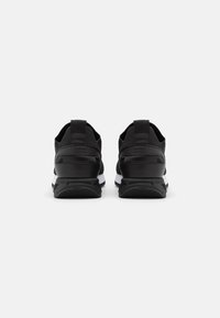 Zapatillas deportivas negras con parte superior de malla y sintético, con una mediasuela blanca, cuello acolchado y tiradores en el talón para facilitar su puesta.