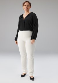 Zwarte blouse met V-hals en lange mouwen, gecombineerd met witte nauwsluitende broek en zwarte puntschoenen. Soepele stof, eenvoudig ontwerp.