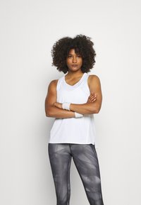 Top técnico blanco de ajuste relajado, combinado con leggings grises con un patrón geométrico y una cinturilla elástica.