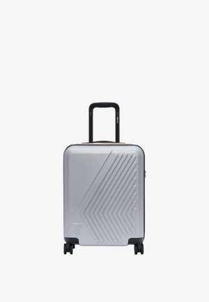 Valise rigide argentée avec des lignes diagonales en relief, poignée télescopique noire et quatre roues pivotantes noires sur fond blanc.