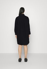 Mörk marinblå oversized skjortklänning med knäppkrage och långa ärmar, med rak passform och sidofickor. Bärs med svarta skor.