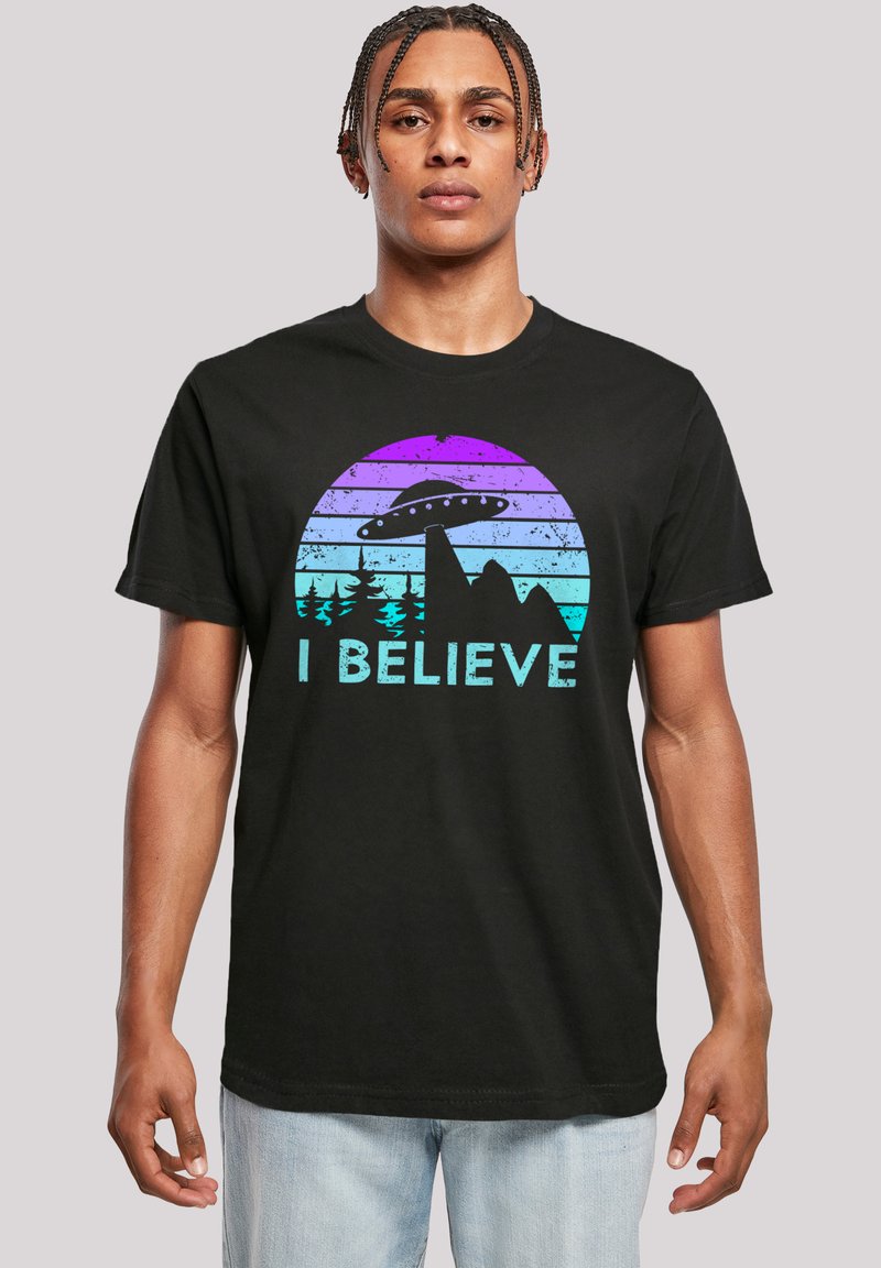 Black cotton t-shirt featuring a graphic design with mountains, a UFO, and the text "I BELIEVE" in blue against a gradient circle.