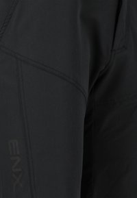 Mustat ulkoiluhousut, joissa on sileä, matta pinta ja erottuvat tikkauskuviot sekä hillityllä sävyllä painettu logo.