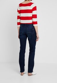 Röd och gräddstripad korttröja med trekvartslånga ärmar, ihop med mörkblå raka jeans och vita slip-on skor.