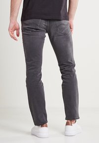 Tmavě šedé džíny s úzkým střihem, s zadními kapsami a kontrastním prošíváním, v kombinaci s bílými teniskami.