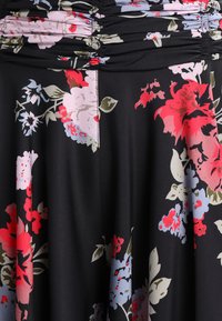 Schwarzer Stoff mit floralem Muster, der rote, rosa und blaue Blumen mit grünen Blättern zeigt, akzentuiert durch geraffte Textur am oberen Rand und fließendes Design.