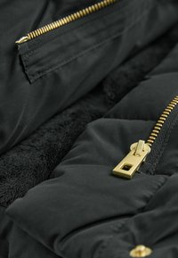 Jachetă puffer neagră cu un interior moale și texturat, fermoare din metal auriu și un material exterior neted, dotată cu mai multe buzunare cu fermoar.