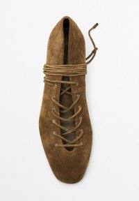 Brune ruskind snørebånd flad sko med spids tå, der har krydsende snørebånd og metaløjer. Glat tekstur, minimalistisk design.