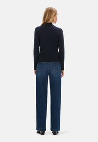 Navyblauer Langarmrollkragenpullover kombiniert mit weit geschnittenen blauen Jeans. Die Jeans verfügen über zwei Gesäßtaschen und einen einfachen Saum.