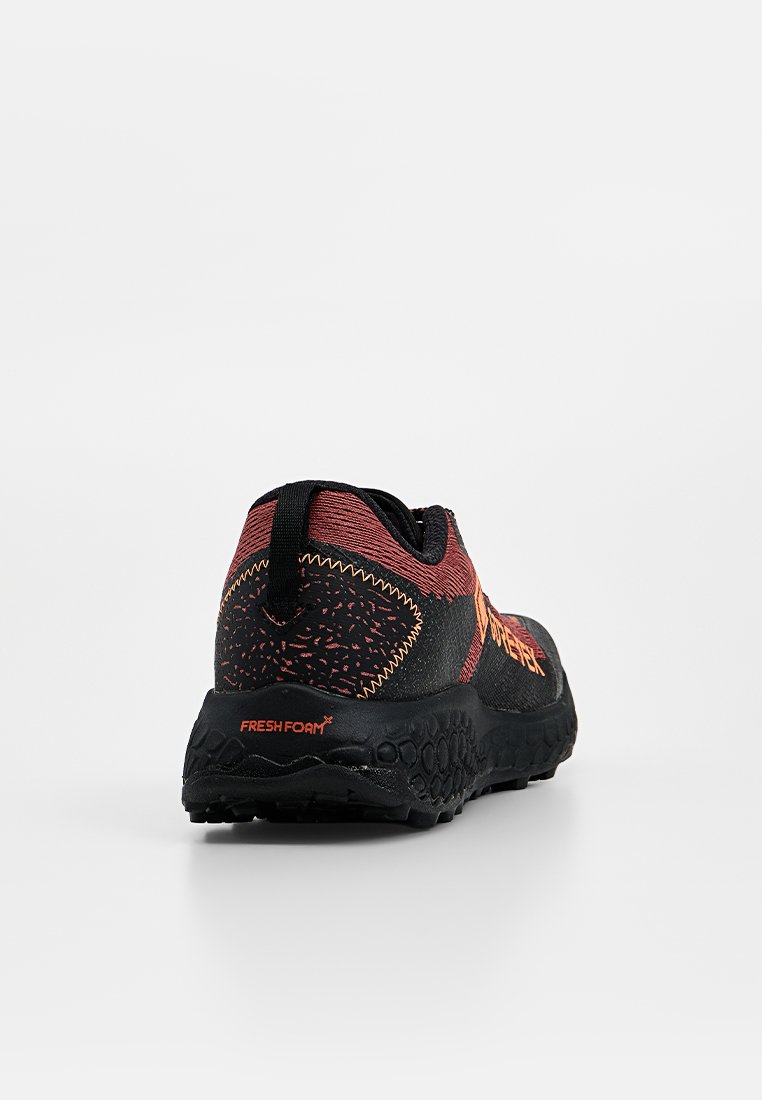 Zapatilla deportiva negra y roja con suela texturizada y la marca "Fresh Foam" en el talón, vista desde atrás sobre un fondo blanco.