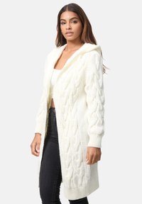 Longue veste en tricot blanche avec capuche, présentant un motif en chevrons, des poignets côtelés et un design à l'avant ouvert.