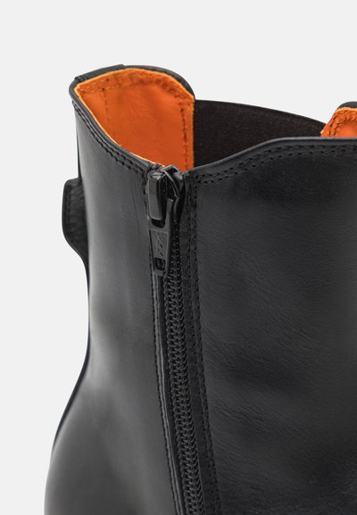 Bota de cuero negra con un interior naranja, que presenta una cremallera lateral y una textura suave. El diseño es elegante con una parte superior redondeada.
