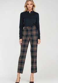 Czarna bluzka z długim rękawem i guzikami, w połączeniu z wzorzystymi spodniami o wysokim stanie w ciemnozielonym, brązowym i niebieskim kolorze, o gładkiej fakturze i prostym kroju nogawek.