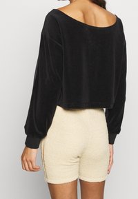 Svart sammet cropped tröja med bred halsringning och långa ärmar, parat med beige, strukturerade shorts. Tröjan har ribbade muddar.