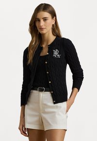 Cardigan noir en tricot avec un motif en câble, doté d'un col rond, d'une fermeture à boutons et d'un logo brodé sur la poitrine.