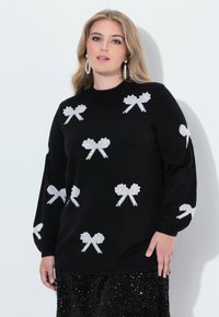 Czarny sweter dzianinowy z białymi wzorami w kokardki, okrągły dekolt i długie rękawy. Materiał wydaje się gładki z lekko luźnym krojem.