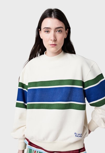 Krémová mikina s horizontálnymi pruhmi v zelenej a modrej farbe. Má voľný strih, ribbované manžety a vyšívaný text na leme.