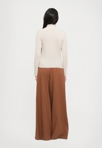 Lys beige langermet genser med høy hals, kombinert med viddebrune bukser, som viser en jevn tekstur og avslappet passform.