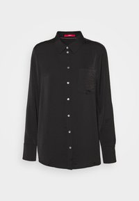 Chemise noire à manches longues, avec des boutons, en tissu léger et texturé, dotée d'un col et d'une poche poitrine unique. Présente des accents de boutons en argent.