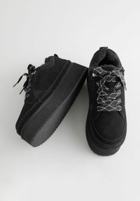 Zapatillas negras con una parte superior de ante texturizado, cordones de patrón en contraste y una suela de goma gruesa y estriada. Forro suave en el interior del zapato.