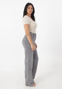 Un body beige de manga corta combinado con unos pantalones vaqueros de mezclilla de corte acampanado de talle alto en un gris claro. Textura suave, costuras mínimas, bolsillos traseros funcionales.