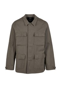 Chaqueta utilitaria color caqui en mezcla de algodón, con corte recto, dos bolsillos en el pecho y cierres de botón en las mangas. Textura suave y diseño minimalista.