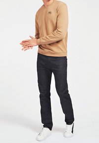 Felpa beige con scollo rotondo, polsini a costine e logo ricamato. Jeans scuri e sneakers bianche completano l'outfit. Fit casual.