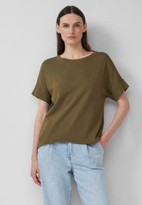 Oliwkowa koszulka z krótkim rękawem, okrągłym dekoltem i podwiniętymi mankietami, wykonana z prążkowanej tkaniny, w połączeniu z jasnoniebieskimi dżinsami.