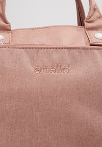 Sac fourre-tout en toile rose avec deux anses supérieures, présentant une surface texturée et un logo de marque embossé "anello" sur le devant.