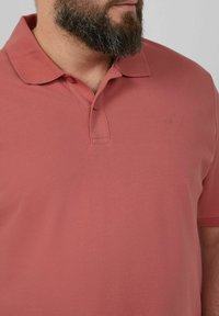 Poloshirt mit kurzen Ärmeln in gedämpfter Korallenfarbe, aus strukturiertem Baumwollstoff. Verfügt über einen klassischen Kragen und ein kleines Logo auf der Brust.