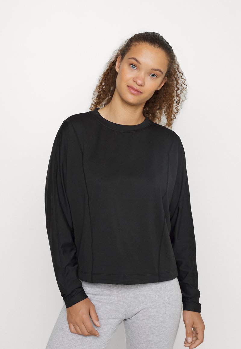 Blusa preta de manga longa com decote redondo e corte solto. O tecido parece suave com um brilho sutil. Combinada com leggings cinzentas.