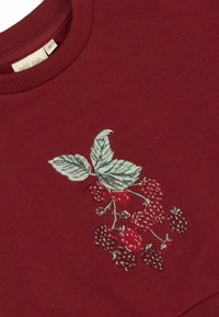 Burgundy pulóver, amelyen hímzett piros és fekete málnák láthatók zöld levelekkel. Puha textúrájú és kerek nyakú.
