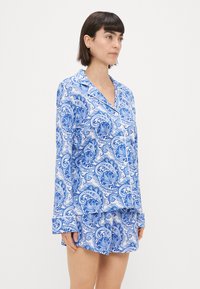 Blue and white patterned pajama set featuring a long-sleeved top with a notch collar and matching shorts with a relaxed fit.