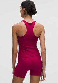 Dopasowany sportowy top na ramiączkach i szorty w intensywnym różowym kolorze. Materiał jest gładki o elastycznej teksturze, z wycięciem w kształcie litery V i geometrycznymi szwami.