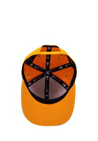 Pomarańczowa czapka bejsbolowa z czarnym daszkiem, wyposażona w osiem otworów wentylacyjnych oraz podszewkę wewnętrzną z logo i okrągłym wzorem.