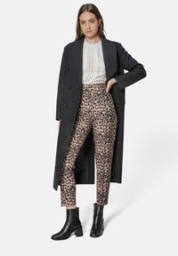 Black long coat over a white textured blouse and pink leopard-print pants. Black ankle boots with a block heel.