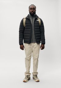 Casaco puffer preto, camada interna cinza, calças cargo bege e ténis bege com detalhes em roxo. Mochila com alças bege.