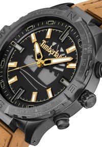 Orologio analogico nero e oro con quadrante nero testurizzato, grandi indicatori e cinturino in pelle marrone. Include dettagli cronografici e marcature della bussola.