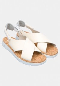 Valkoiset sandaalit, joissa on ristikkäinen strap-design, korkkipohja ja valkoinen kumipohja. Varustettu säädettävillä kantaremmeillä turvallisen istuvuuden saavuttamiseksi.