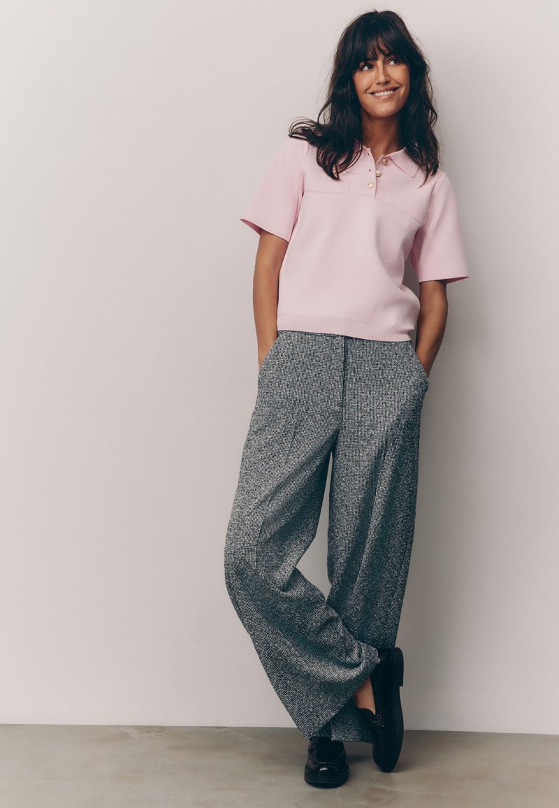 Roze polo shirt met korte mouwen, met een geribde zoom en twee borstzakken, gecombineerd met brede grijze geprinte broeken en zwarte schoenen.