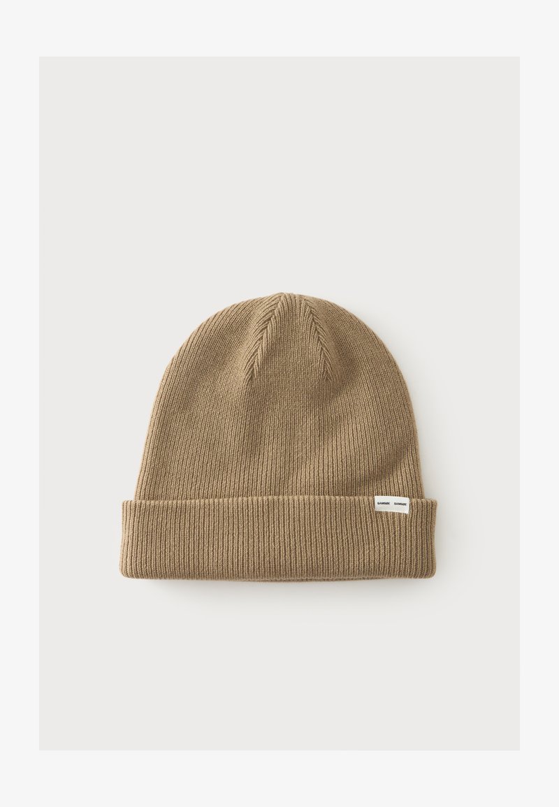 Bonnet en maille brun clair avec un revers plié et une petite étiquette blanche sur le poignet, sur un fond clair uni.